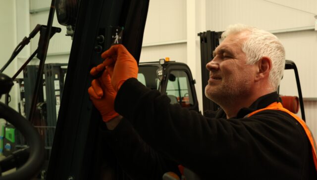Gary Kelly installs a Safety Shield indicator onto a black forklift truck