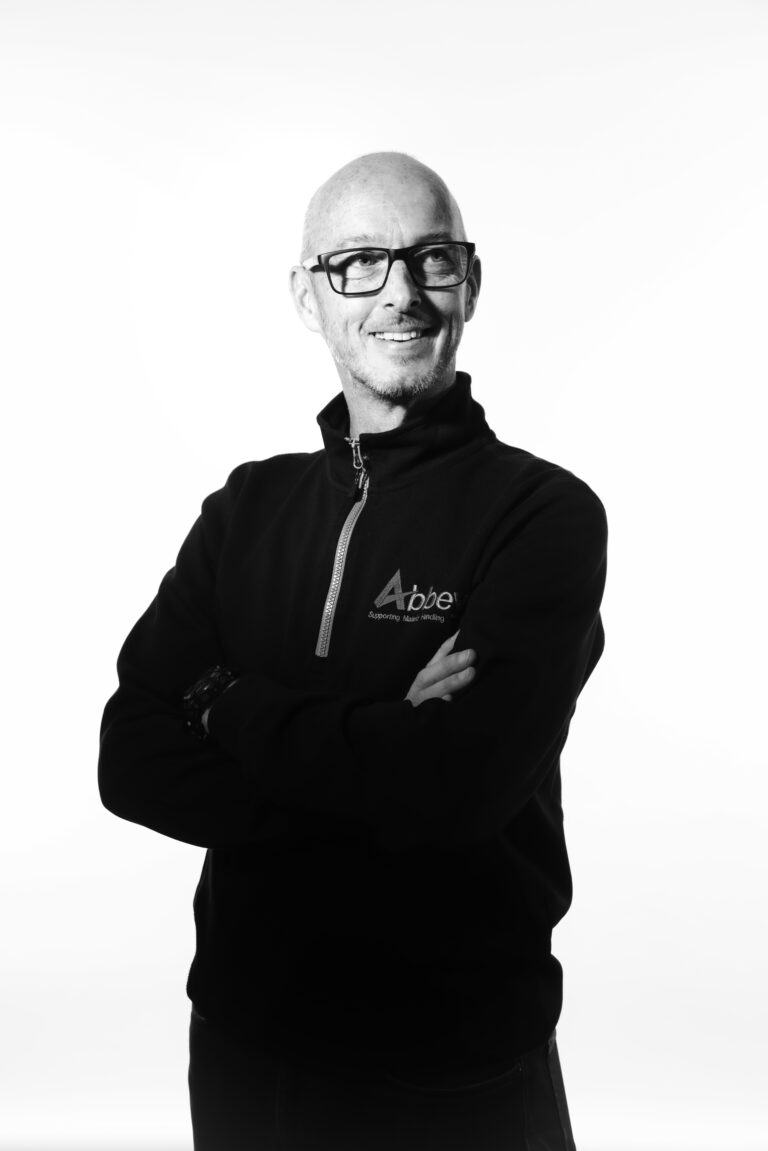 richard kynaston is standing with his arms folded in an abbey-branded jumper looking happily to his left.