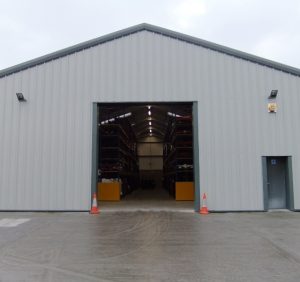 a large grey warehouse with a triangle shaped roof, with the central fold up door completely open
