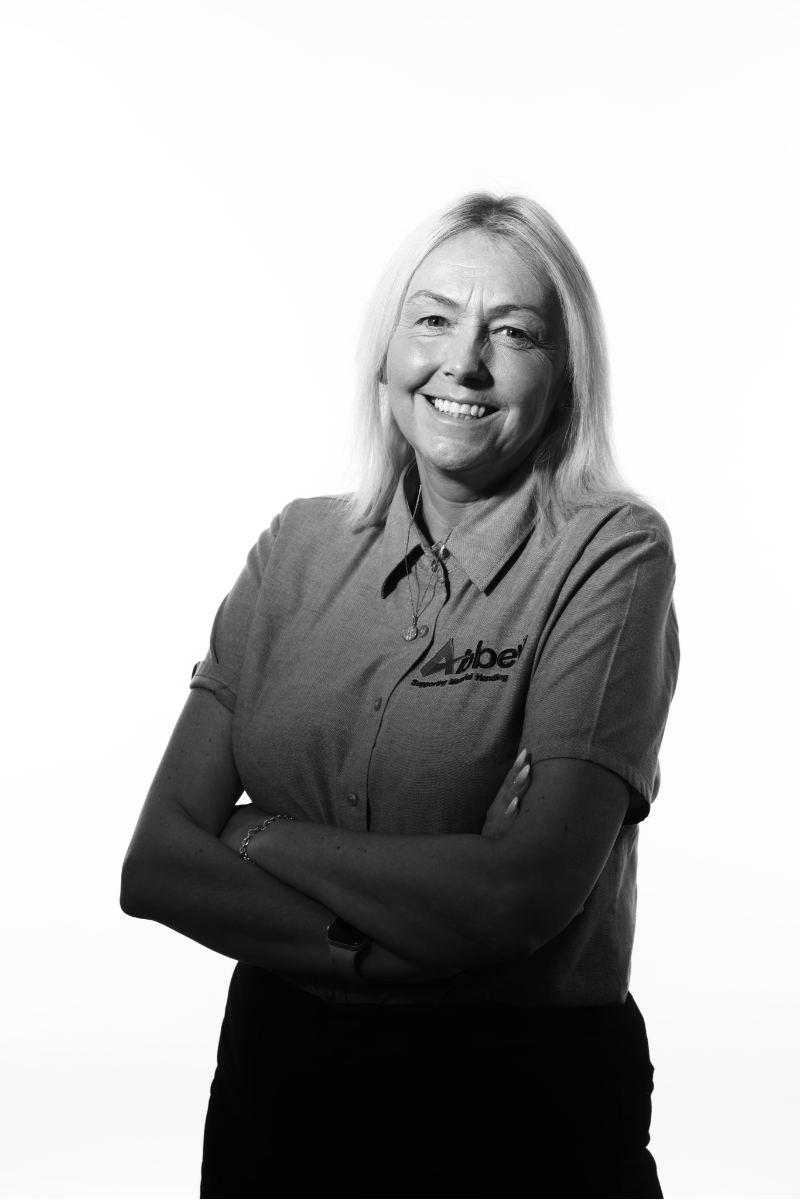 angela owen is smiling at the camera wearing a grey abbey shirt with a black and white overaly