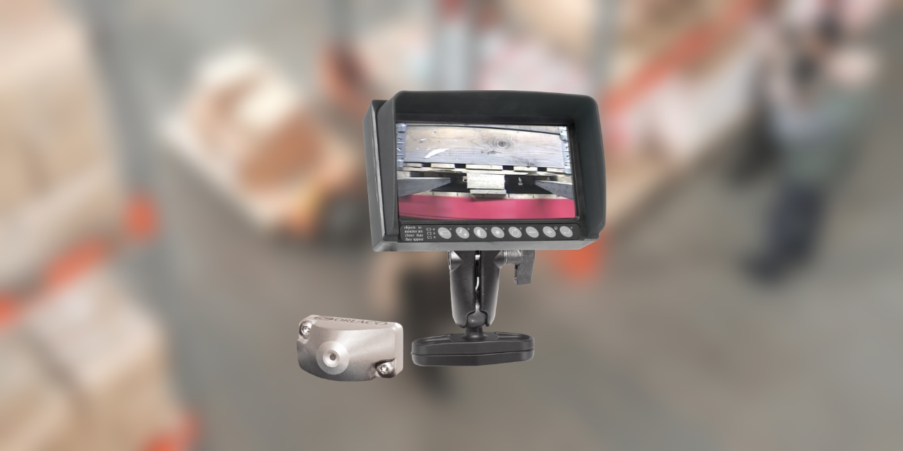 the silver orlaco cph forklift safety camera and black rled monitor are seen clearly in front of a blurred background