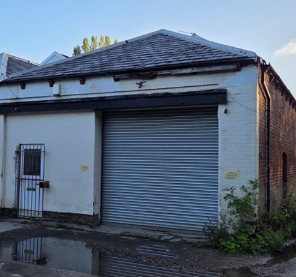 a crumbling brick garage with a grey shutter door and a tiled, triangular roof