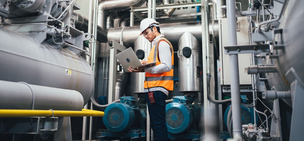 we see a worker wearing an orange hi-vis jacket surrounded by metal container around a nuclear reactor