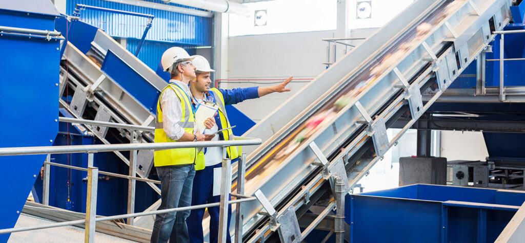 two operators in hi-vis jackets and helmets are talking inside a large warehouse