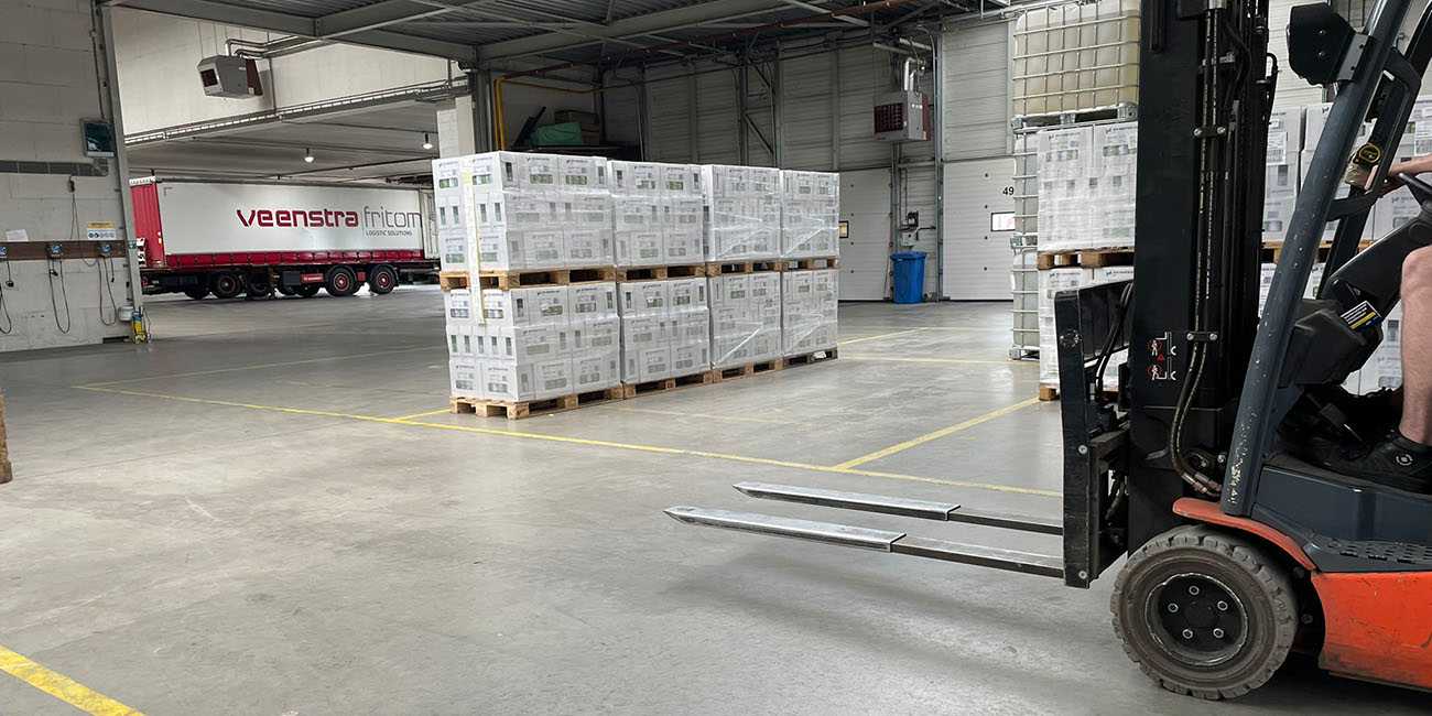 kooi reachforks are attached to the front of a red forktruck as it drives through a spacious warehouse