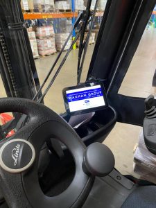 The inside of a black forklift truck holds a tablet displaying the waxman group portal homescreen