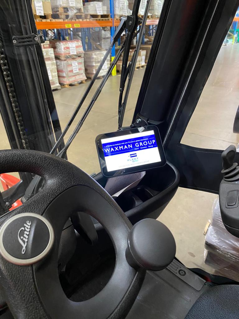 The inside of a black forklift truck holds a tablet displaying the waxman group portal homescreen